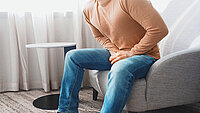 Urologenzentrum Wien - Penisspitzenschmerz: Mann sitzt und hält sich schmerzerfüllt den Unterleib.
