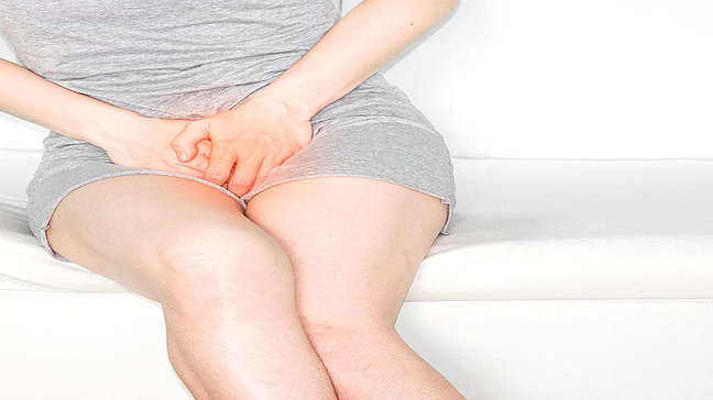 Dyspareunie - Beschwerden im Genitalbereich Urologenzentrum Wien - Dyspareunie bei einer Frau, sitzend auf einem Sofa, zeigt Beschwerden im Genitalbereich.